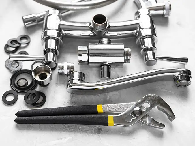 Disassembled chrome sink faucet with plumbing wrench